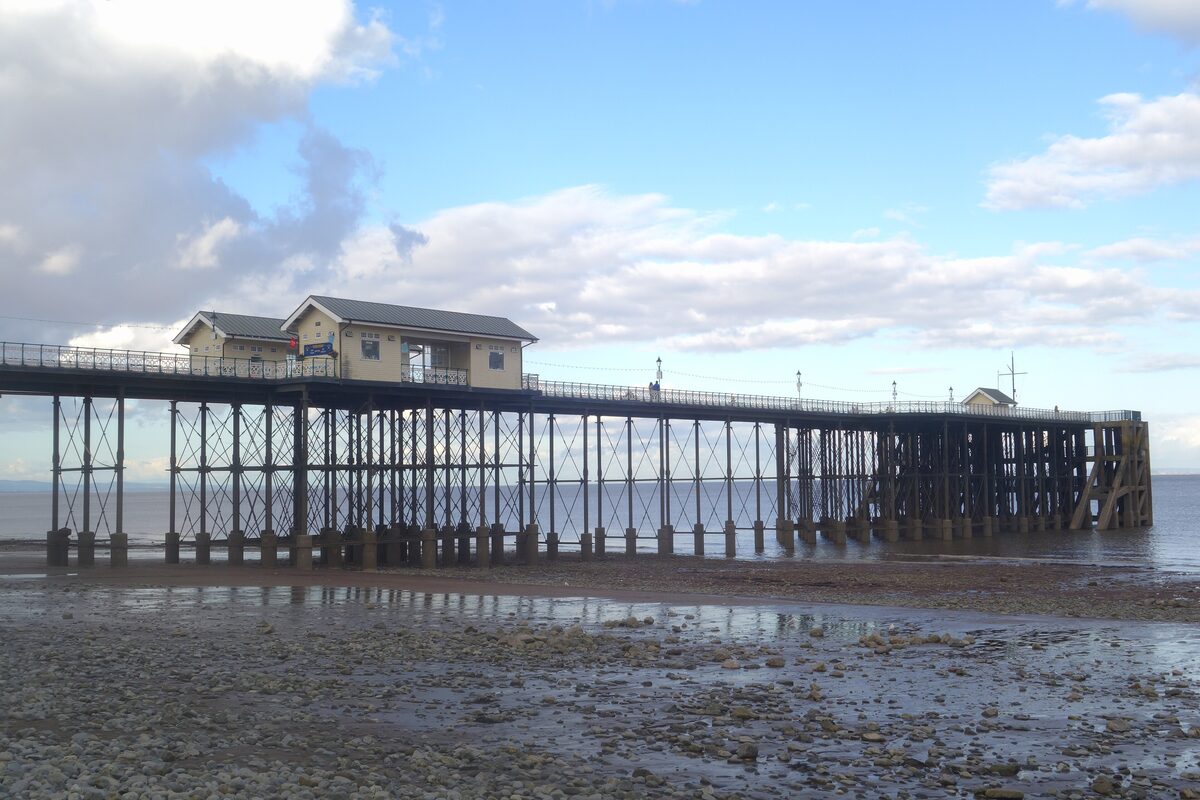 Penarth Pier on its iron legs stretching out over the wet sand at low tide, with its pavilion and a big sky