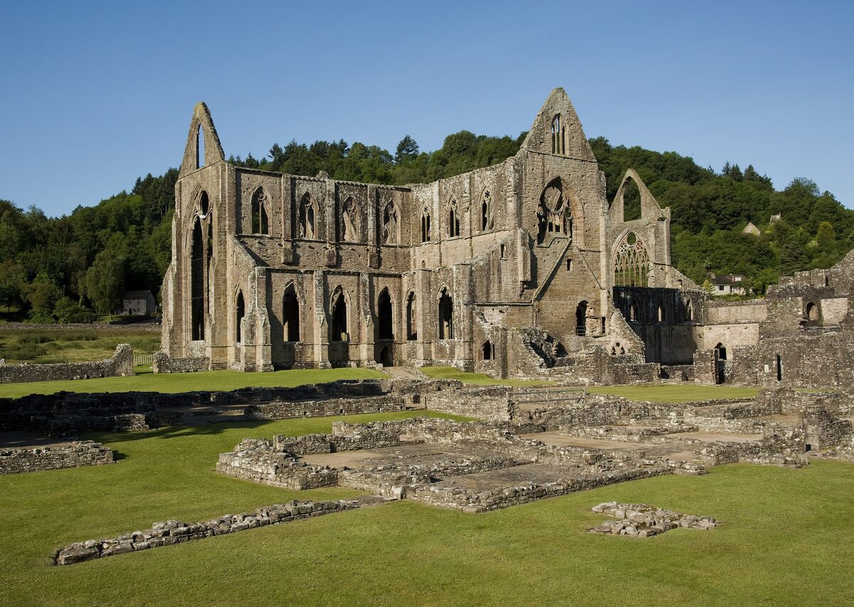 The roofless Gothic ruins of Tintern Abbey with tall arched windows, beside a green lawn