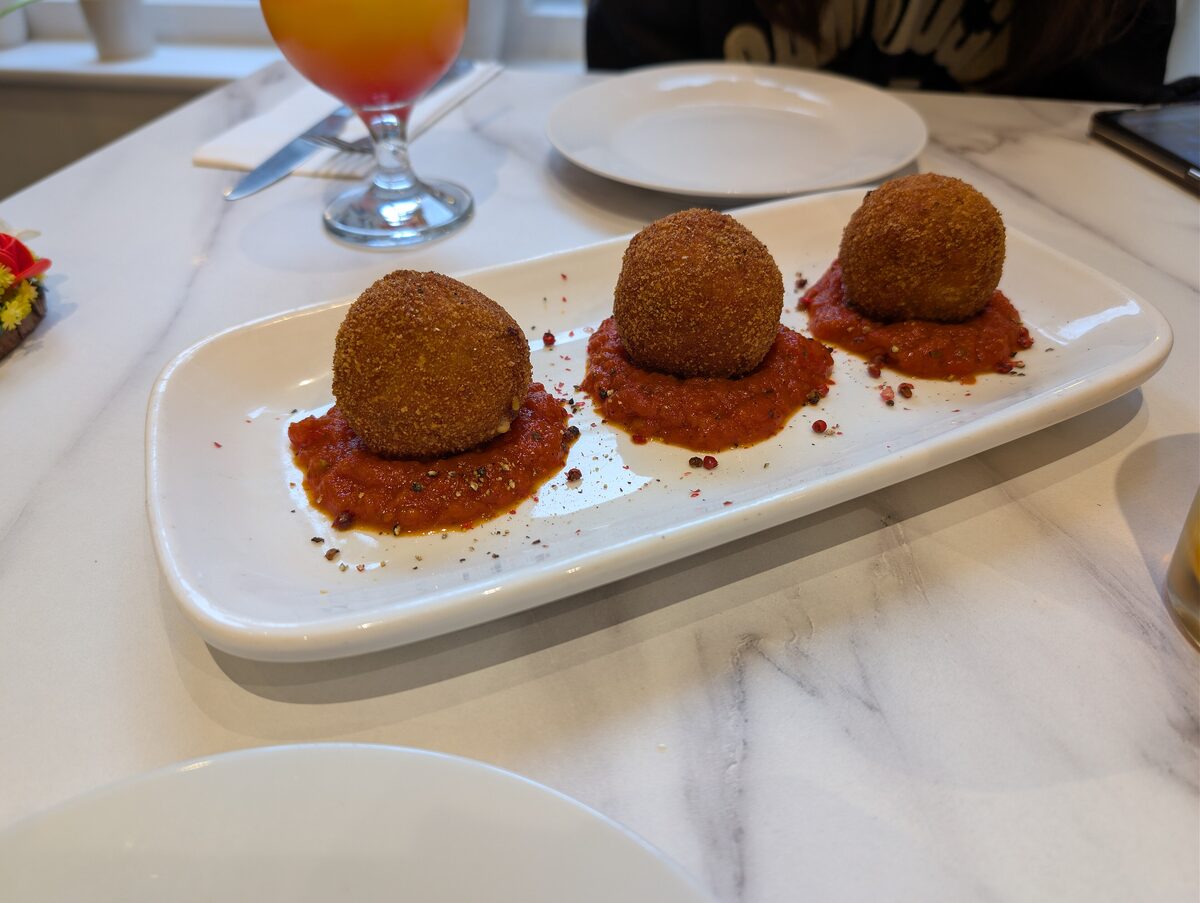 Three golden fried arancini on a white plate with a red ragu sauce underneath