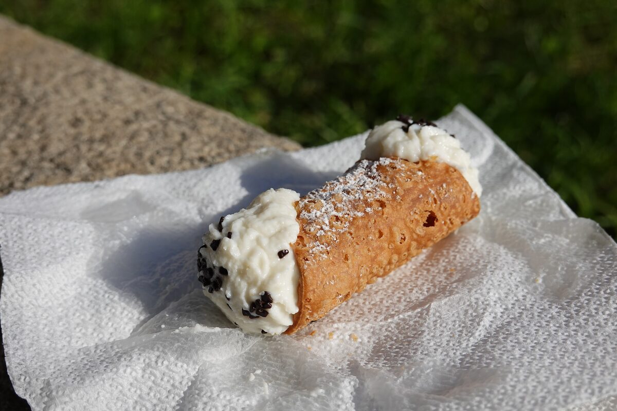 A cannolo with a crisp fried shell, ricotta filling at both ends and a dusting of sugar on a paper napkin