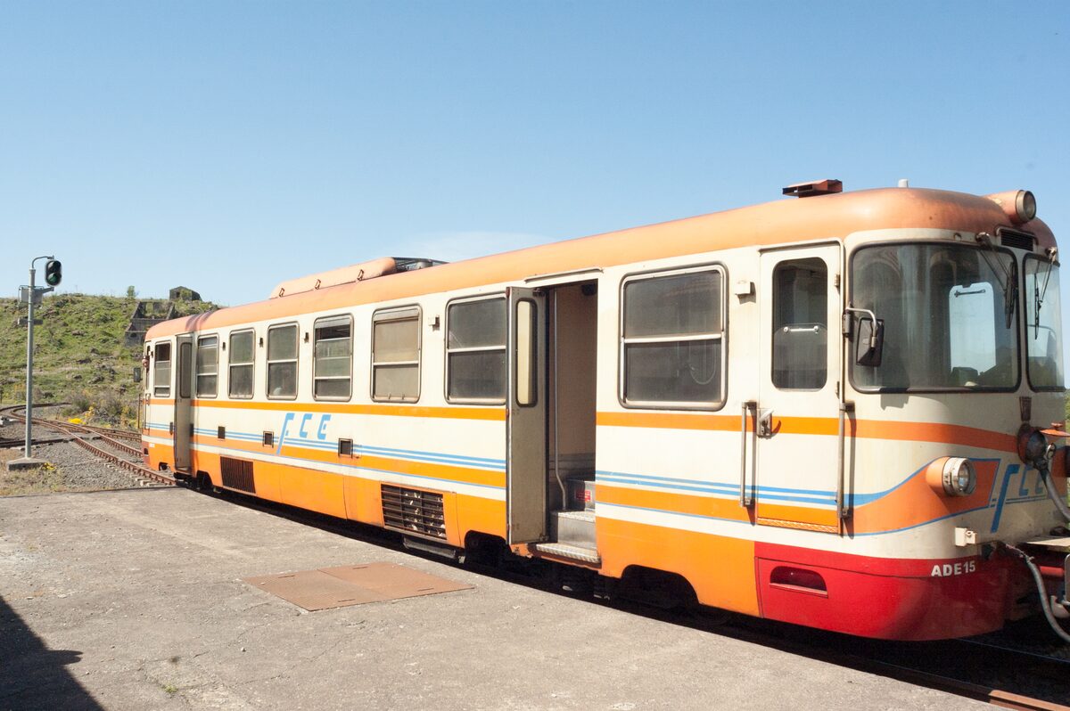 Orange and white Circumetnea train standing at a station, the narrow-gauge line that circles Mount Etna