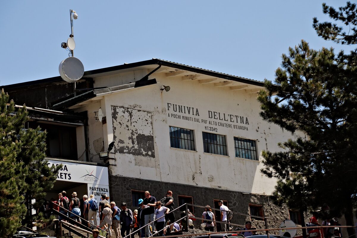 The white Funivia dell'Etna station at Rifugio Sapienza, with a crowd waiting on the steps below the pines
