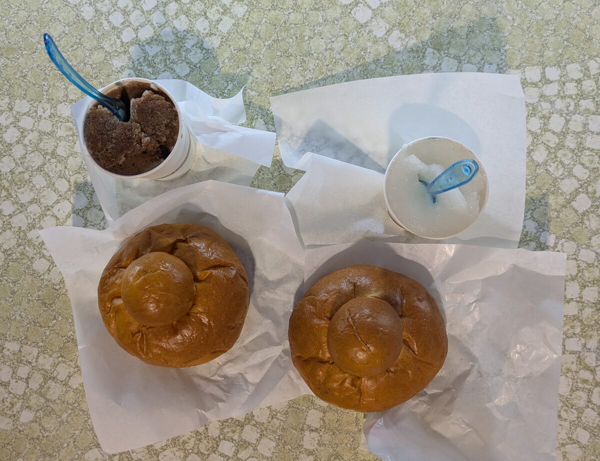 Granita in paper cups beside two round brioche buns on a paper napkin