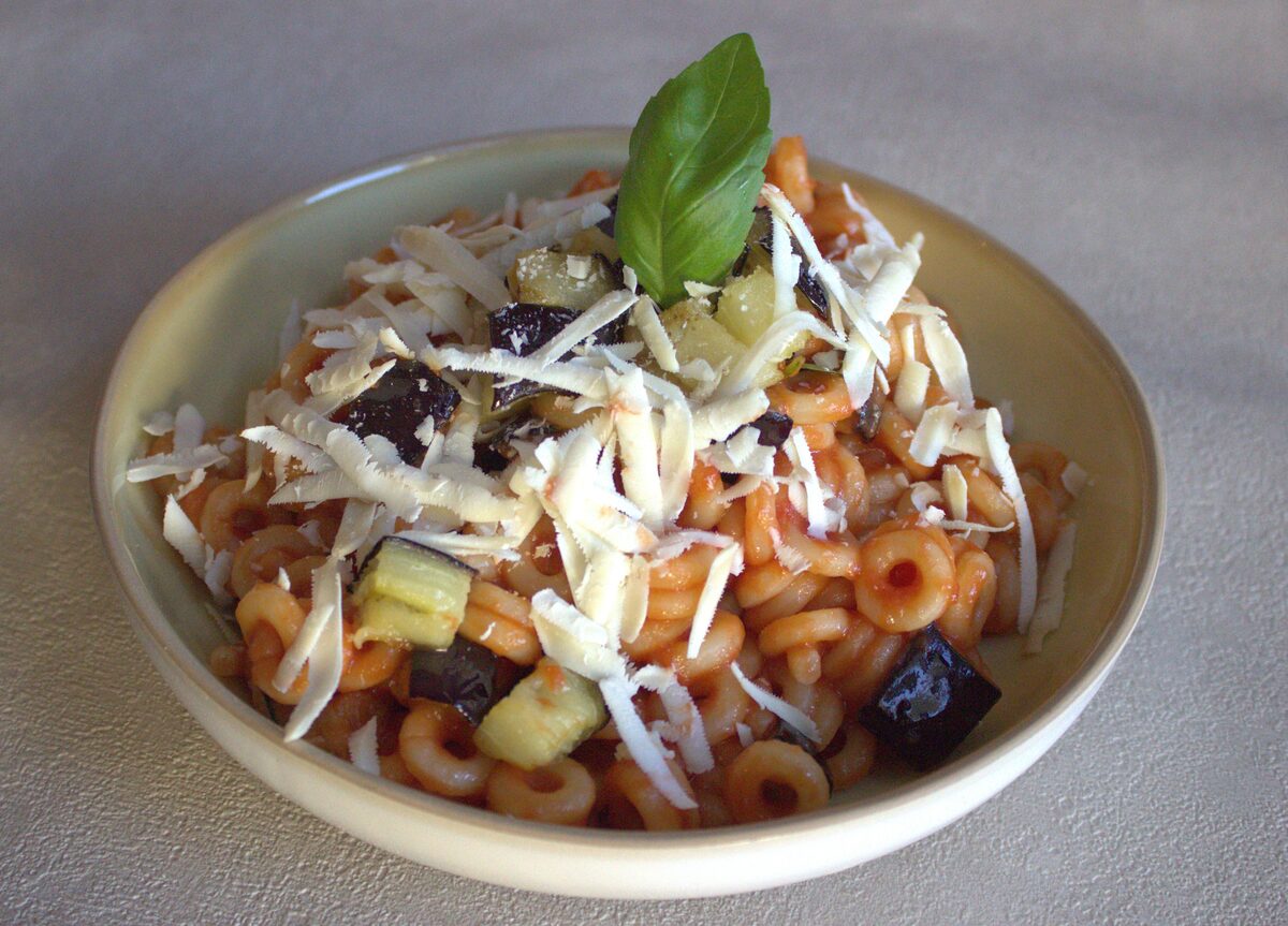 Bowl of pasta alla Norma with tomato sauce, fried aubergine cubes, grated ricotta salata and a basil leaf