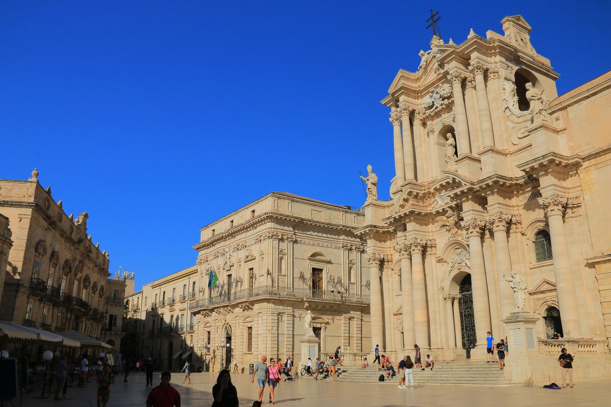 The baroque facade of Syracuse Cathedral on Piazza Duomo in Ortigia, under a deep blue sky