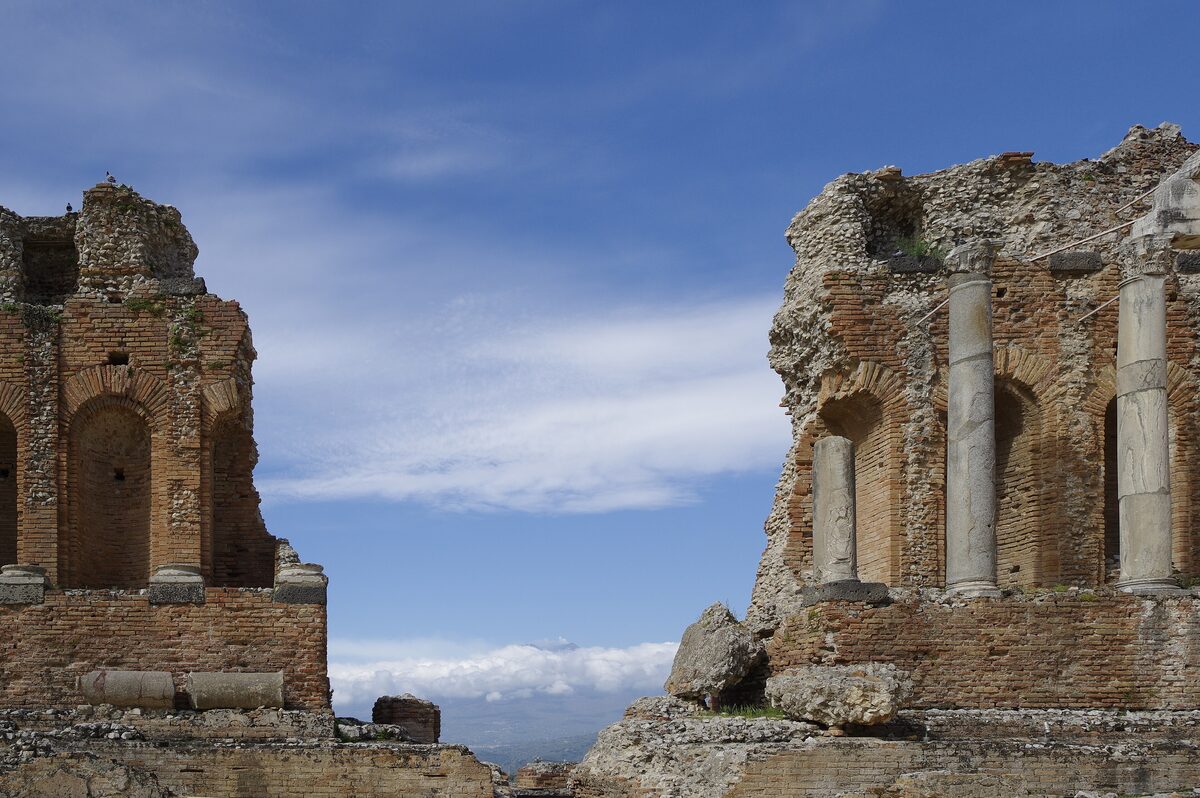 Brick and stone arches and columns of the ancient theatre of Taormina against a blue sky