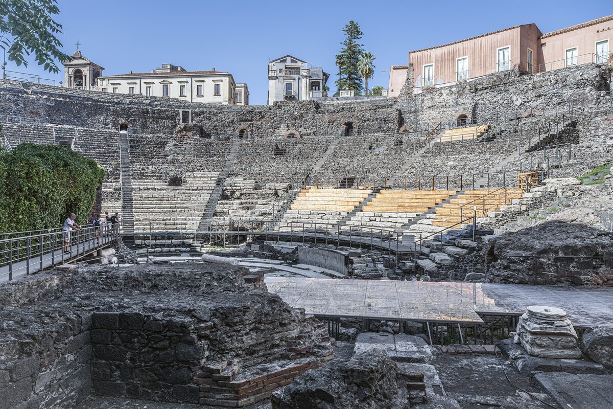 Stone seats and arches of the Roman theatre in Catania, with 18th-century palaces rising behind it