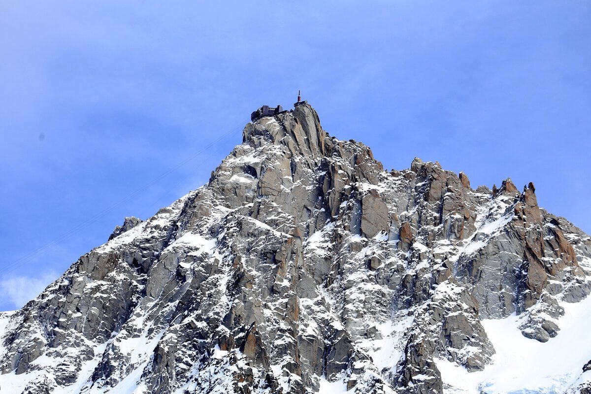 The rocky needle of the Aiguille du Midi with its summit station and antenna, snow on the granite under a blue sky