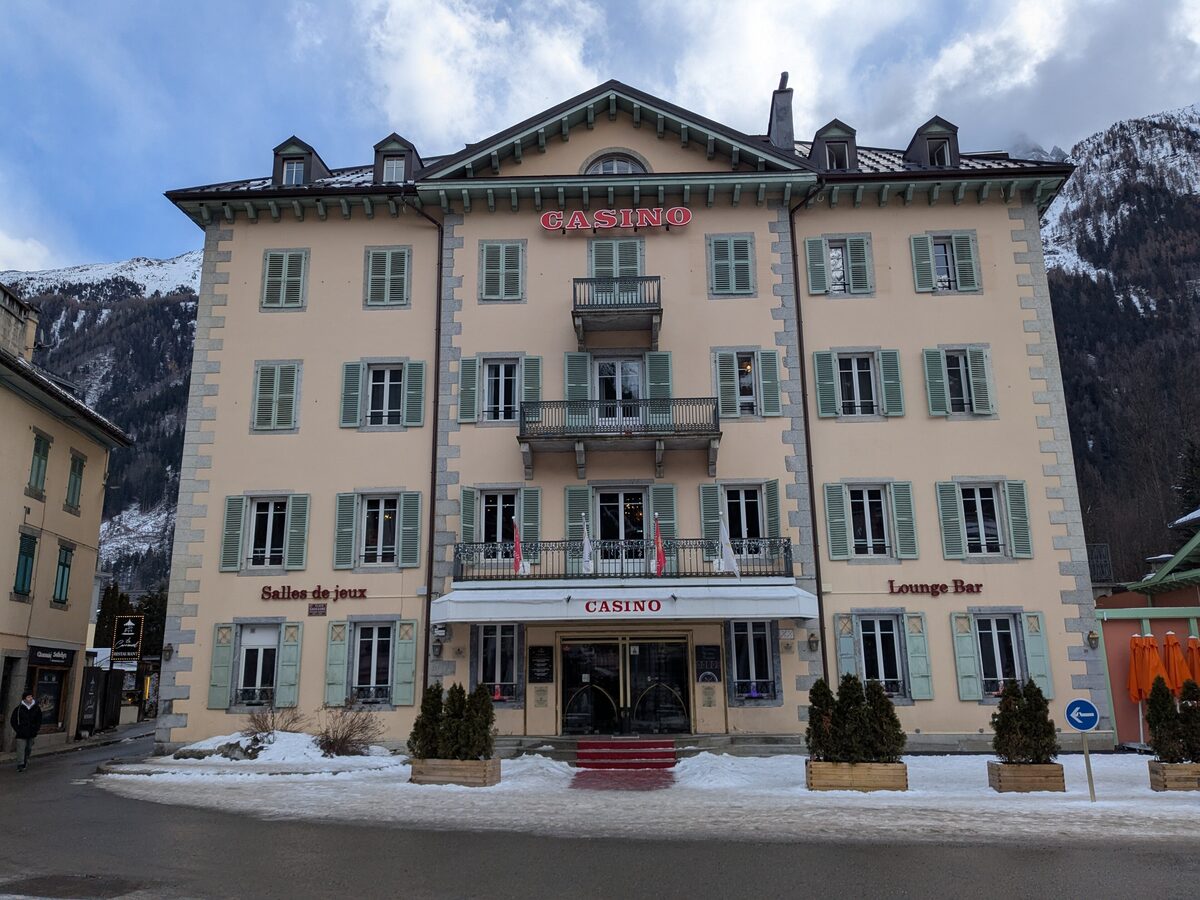 The Casino building in the center of Chamonix with snow on the pavement and snowy slopes rising behind it