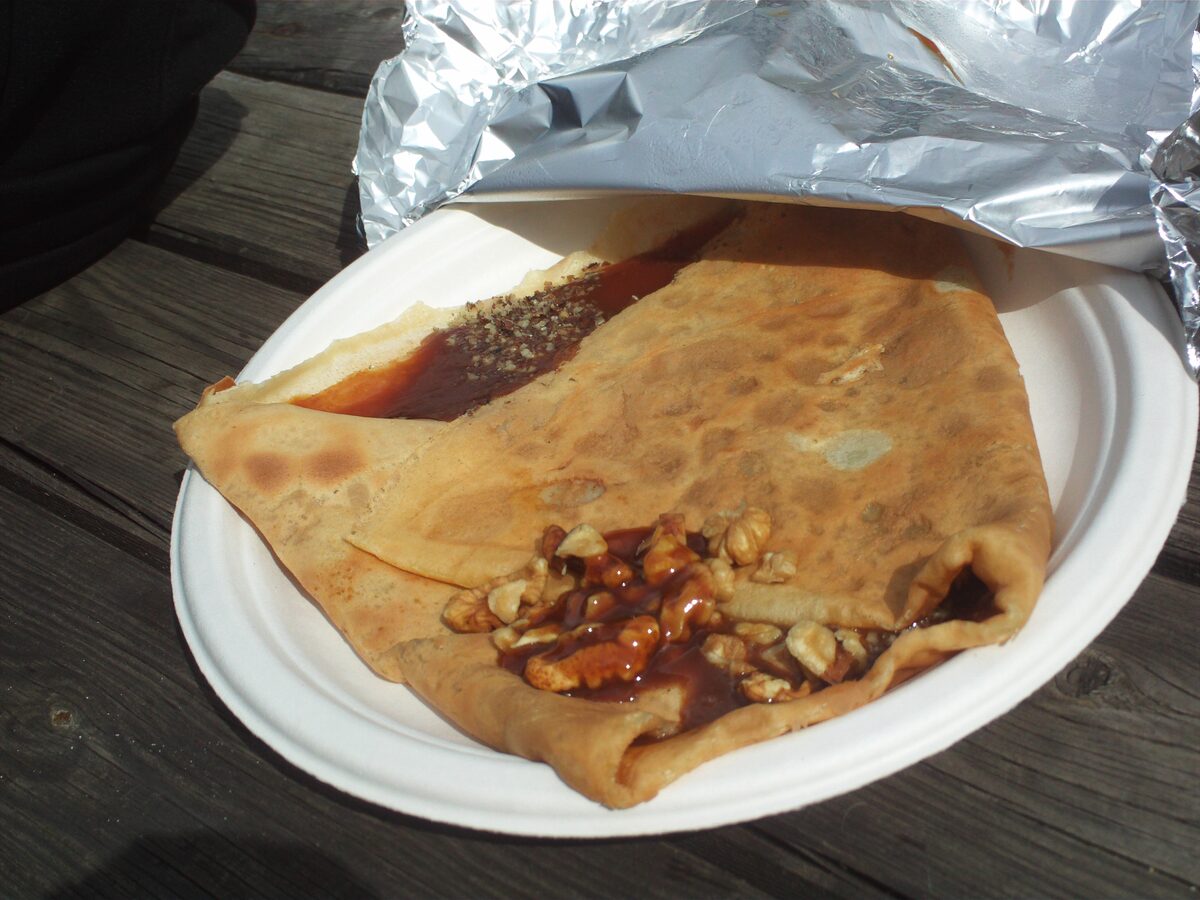 A folded crêpe with caramel and chopped nuts on a paper plate, on a wooden table