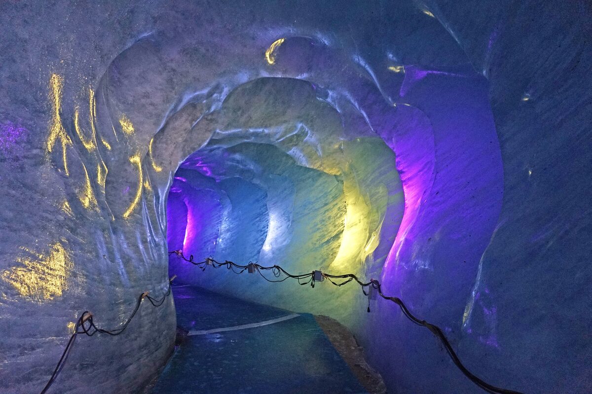 Violet and blue lights inside the ice tunnel of the Mer de Glace cave, with a rope along the floor