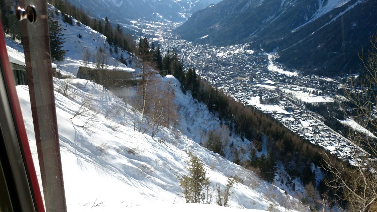 The view from a window of the Montenvers train: snowy slopes and pines falling away to Chamonix far below in the valley