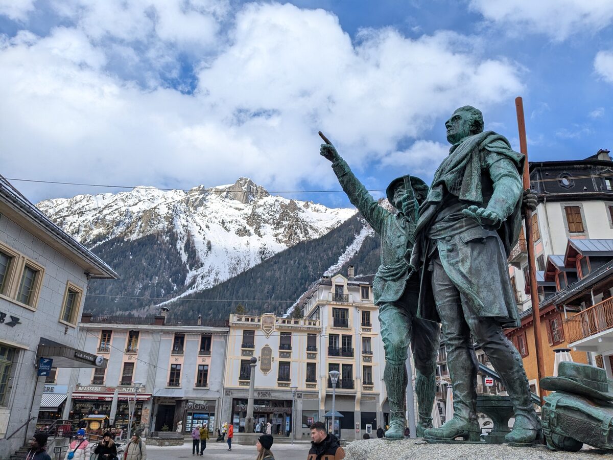 The bronze statue of Jacques Balmat and Horace-Bénédict de Saussure on Place Balmat in Chamonix, with the snowy Brévent behind the rooftops