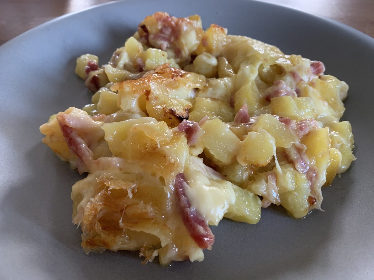A portion of tartiflette on a plate, with potatoes, bacon pieces and melted cheese