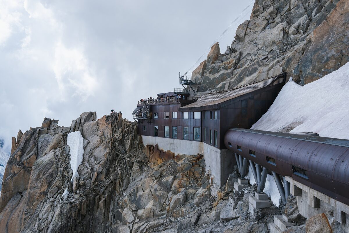 The Aiguille du Midi summit station built into the rock, with the steel tunnel leading out of it and snow on the ledges