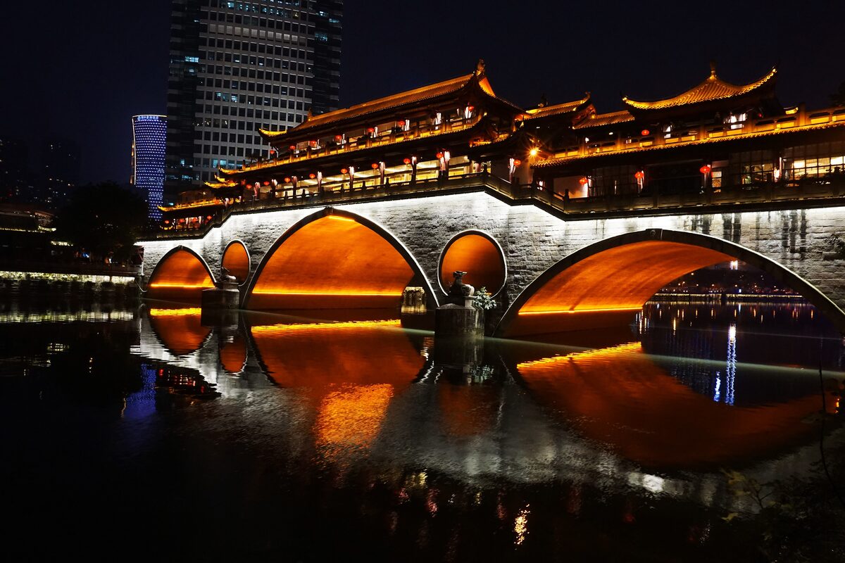 Anshun Bridge lit up at night, its covered pavilion and arches reflected in the Jin River