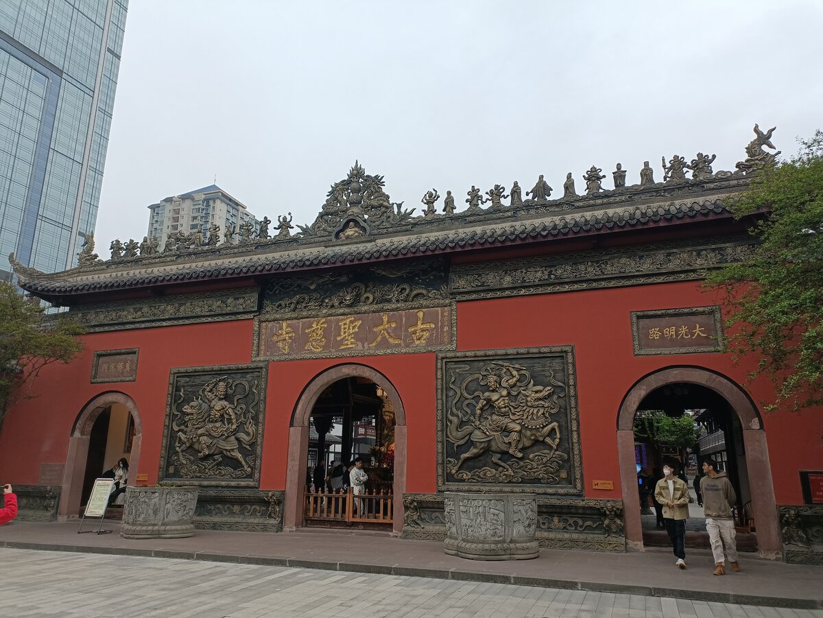 The red three-arched mountain gate of Daci Temple with carved panels, and a glass tower rising behind it