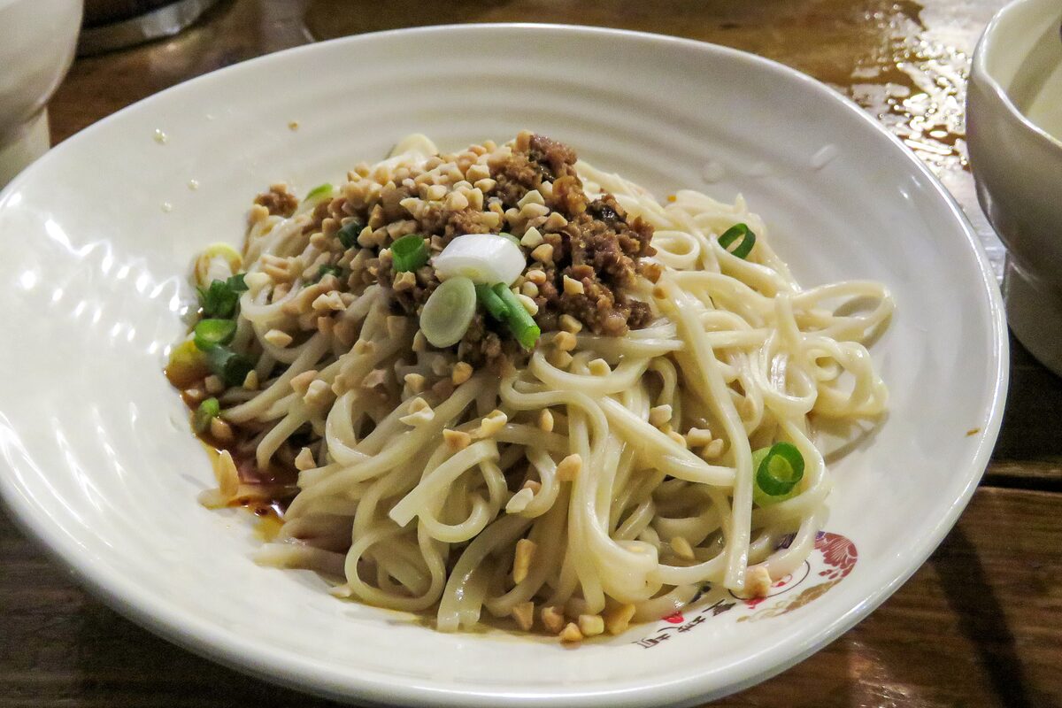 A plate of dan dan noodles with minced pork, peanuts and scallions piled on top