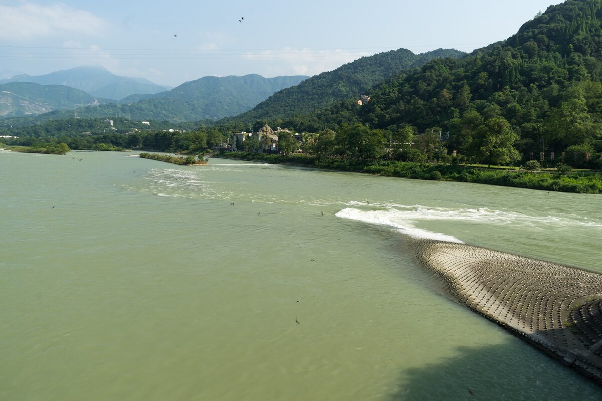 The Yuzui fish-mouth embankment splitting the green Min River at Dujiangyan, with forested hills behind