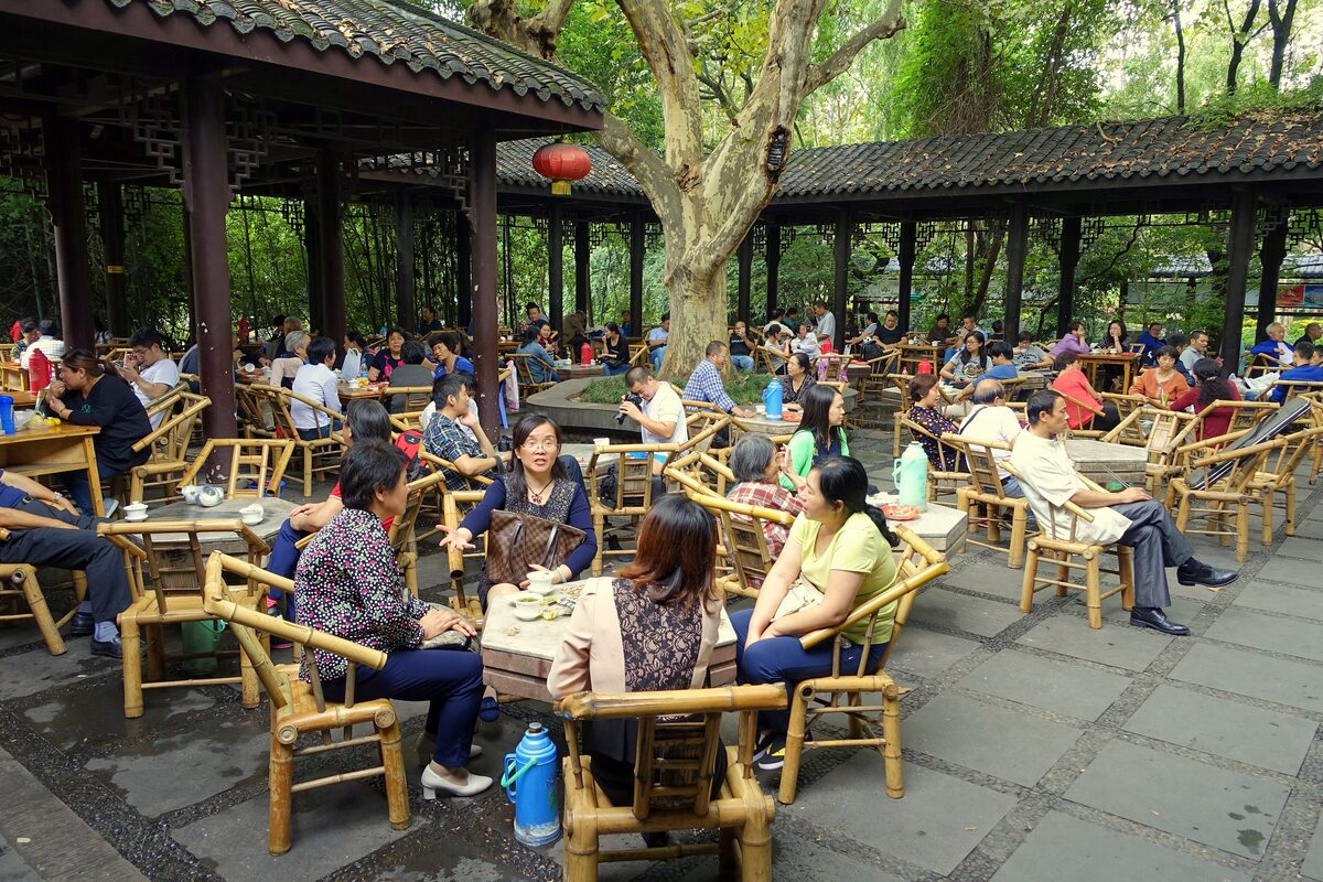 People drinking tea at bamboo chairs and tables under a covered pavilion in a People's Park teahouse