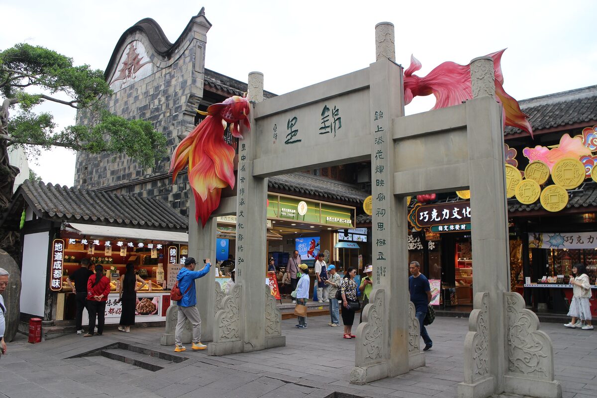 A stone archway with red carp sculptures at the entrance of Jinli Ancient Street, with snack shops on both sides