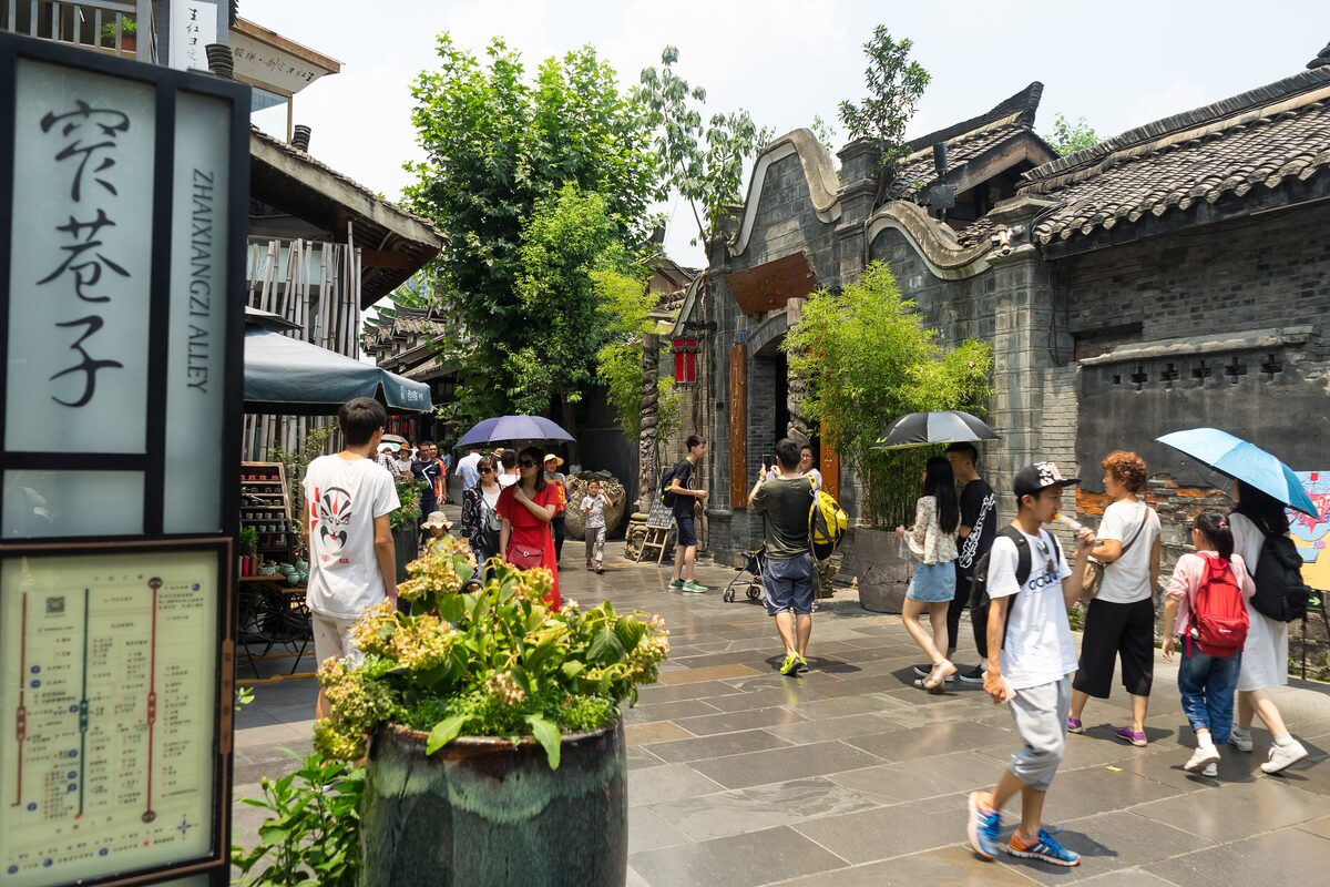Visitors under umbrellas in a paved lane of Kuanzhai Alley, with gray-brick courtyard houses and a map sign