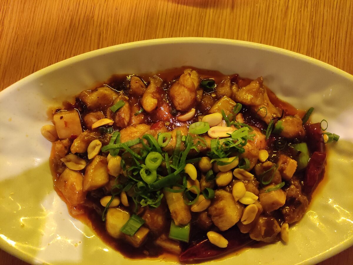 Kung Pao chicken with peanuts, scallions and dried chilies in a glossy sauce on an oval plate