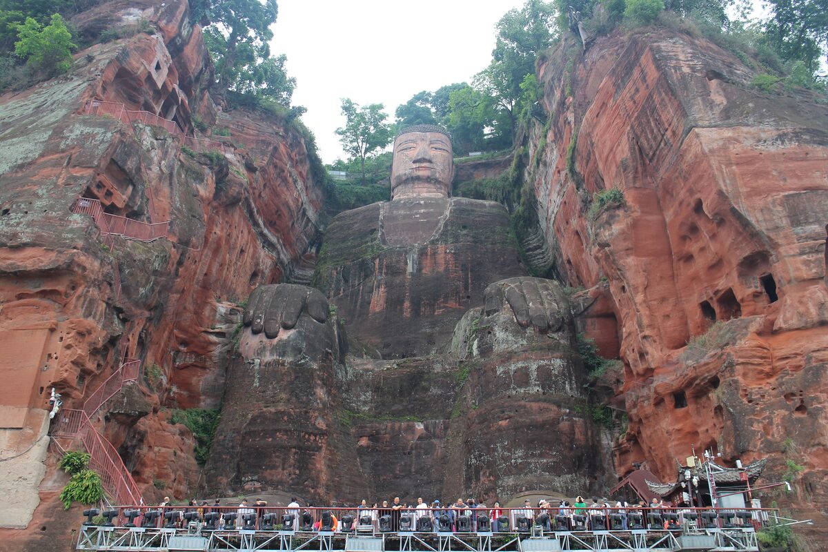 The Leshan Giant Buddha seated in a red sandstone cliff, with visitors on the viewing platform at its feet
