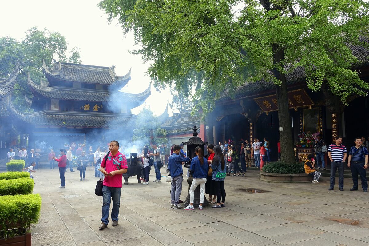 Visitors in a courtyard at Wenshu Monastery with incense smoke drifting in front of a temple hall