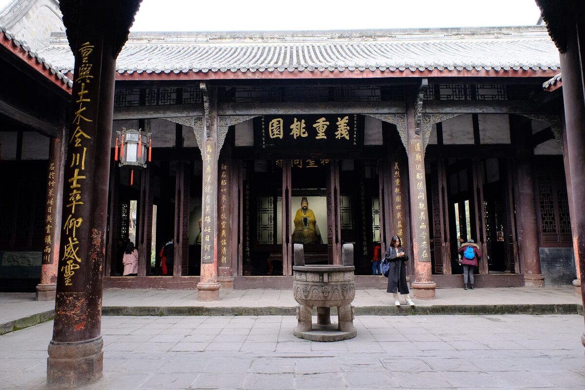 A hall of the Wuhou Shrine with carved wooden pillars and an incense burner in the paved courtyard