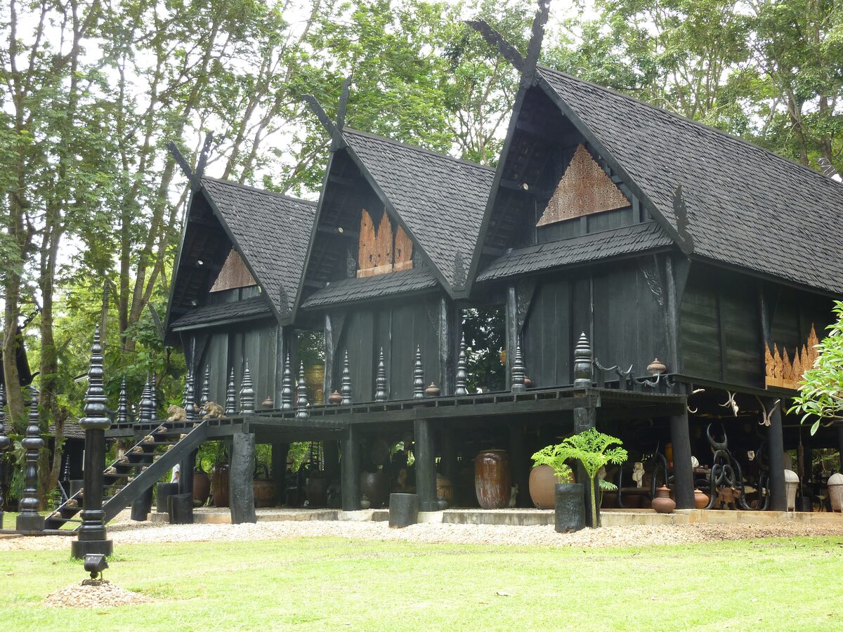 A dark wooden building with a steep roof and carved gables at Baan Dam, the Black House