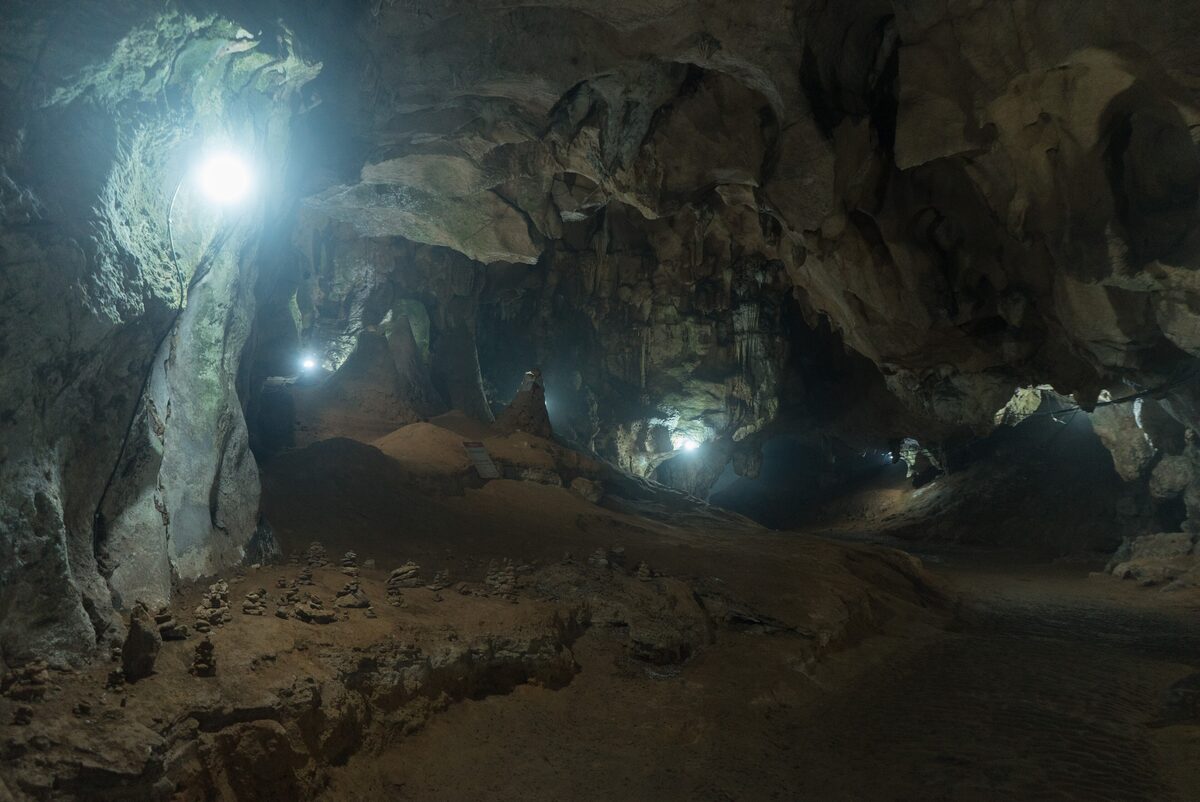 Inside Chiang Dao Cave, a large limestone chamber lit by lamps, with a rocky floor
