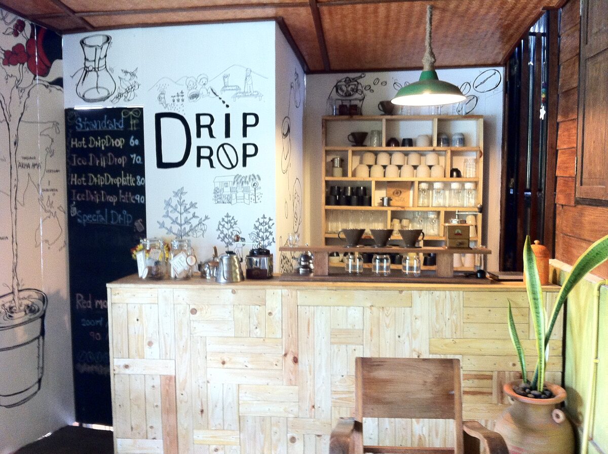A small café counter with pour-over coffee gear on wooden shelves and a chalkboard drip-coffee menu