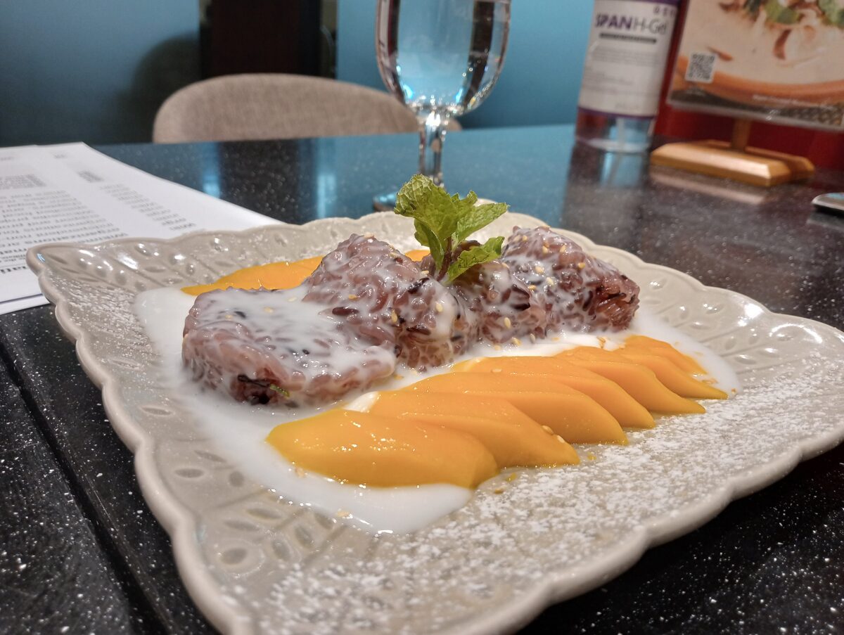 Sliced mango beside a block of sticky rice and coconut sauce on a white plate