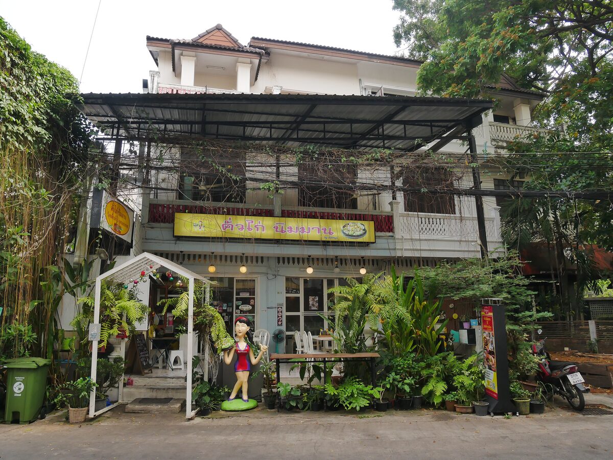 A two-story café house on Nimmanhaemin Road with a small garden of potted plants and a covered terrace
