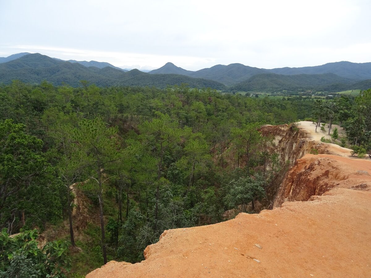 The orange clay ridge of Pai Canyon above pine forest, with blue mountains in the distance