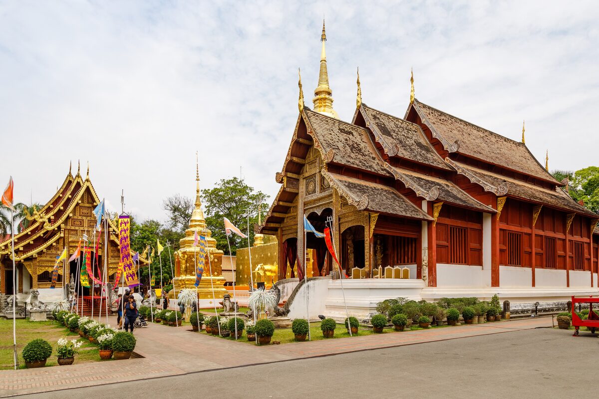 The golden Lanna hall of Wat Phra Singh with its tiered roofs, flags and a gilded chedi beside it
