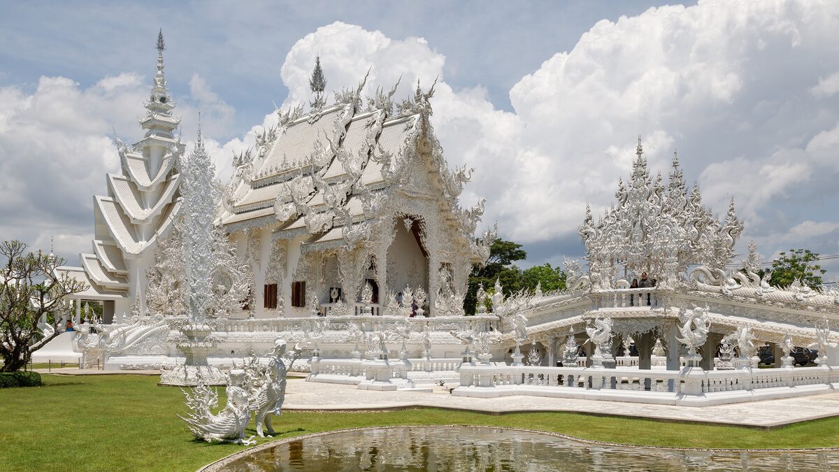 The white temple of Wat Rong Khun in Chiang Rai, with white spires and carved details under a cloudy sky
