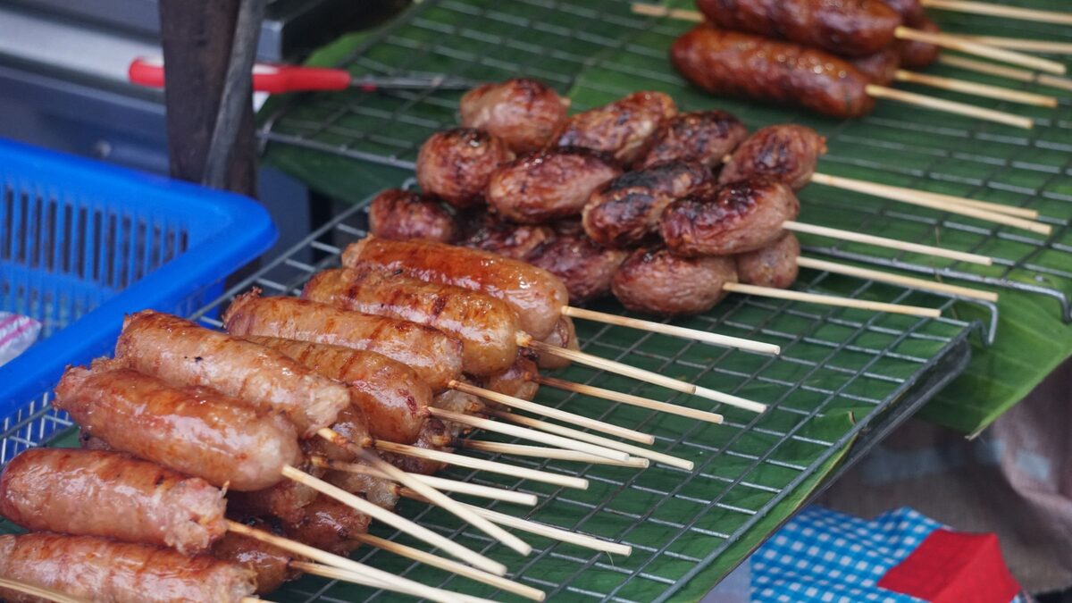 Rows of grilled Chiang Mai sausage on skewers laid on a banana leaf at a street food stall
