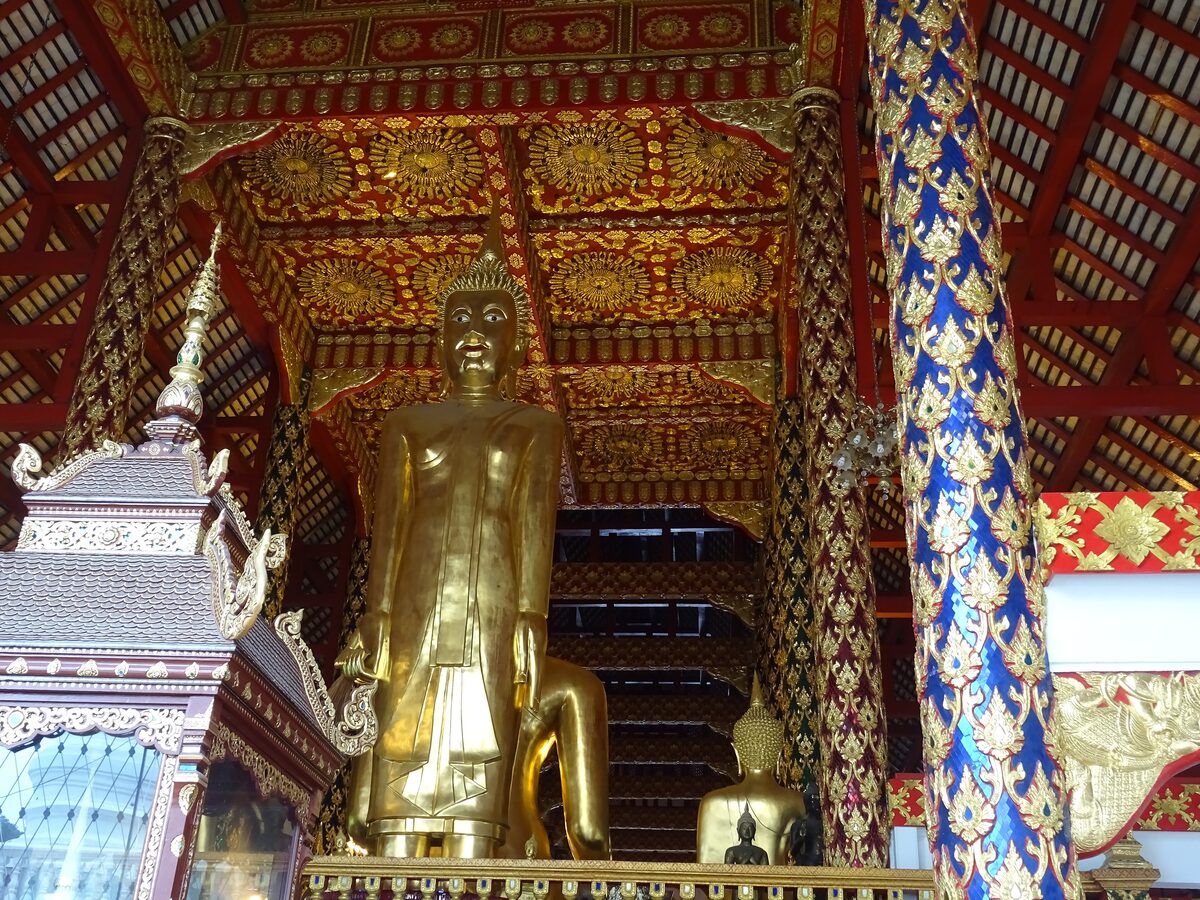 A gilded Buddha statue in a Lanna hall at Wat Suan Dok, under a carved wooden ceiling