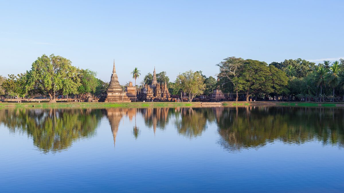 The ruined chedis of Wat Mahathat in Sukhothai Historical Park, reflected in a still lake