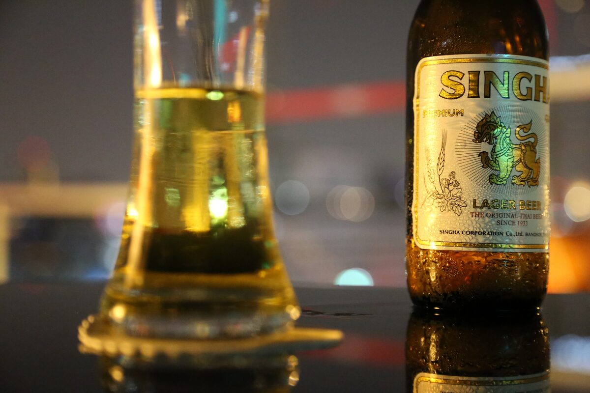 A glass of Singha beer beside a bottle on a bar at night