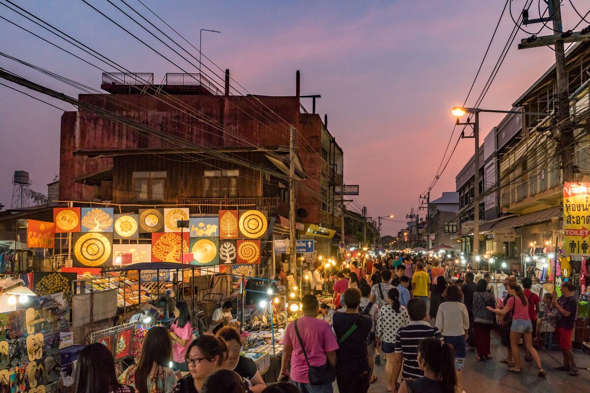 A Saturday evening street market at dusk, with craft stalls lit up and a crowd walking between old shophouses