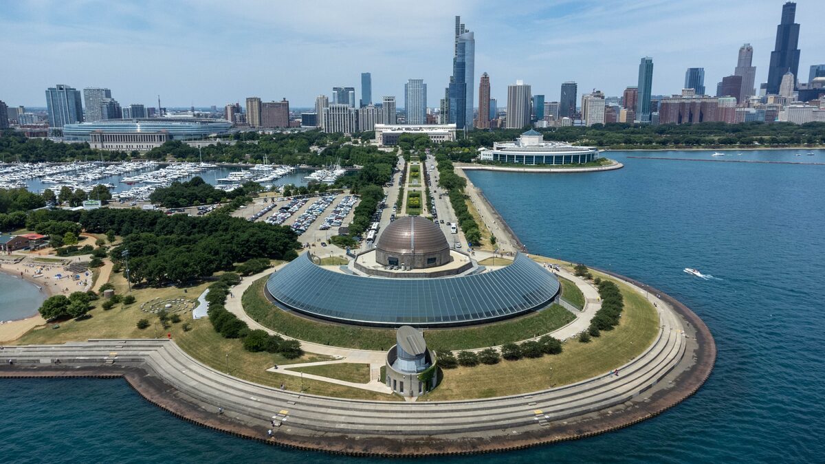 Aerial view of the domed Adler Planetarium on its peninsula in Lake Michigan, with the skyline behind