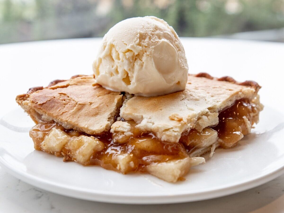 A slice of apple pie with a golden crust and a scoop of vanilla ice cream on top