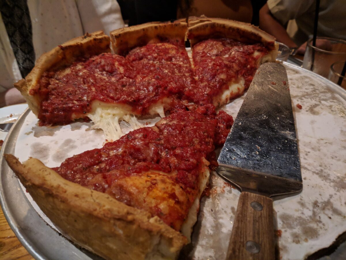 A deep-dish pizza with a thick crust and chunky tomato sauce, cut into slices