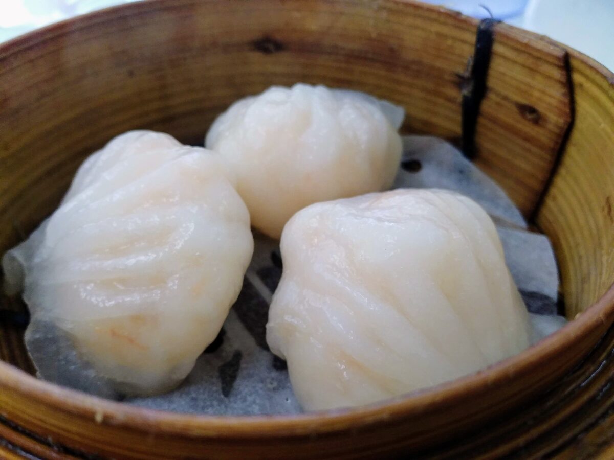 Three har gow dumplings with translucent wrappers in a bamboo steamer