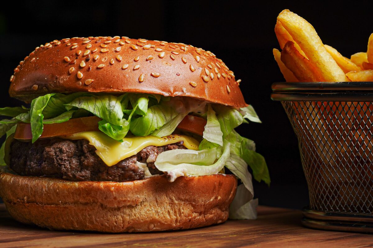 A cheeseburger with lettuce and tomato on a sesame bun, beside a basket of fries
