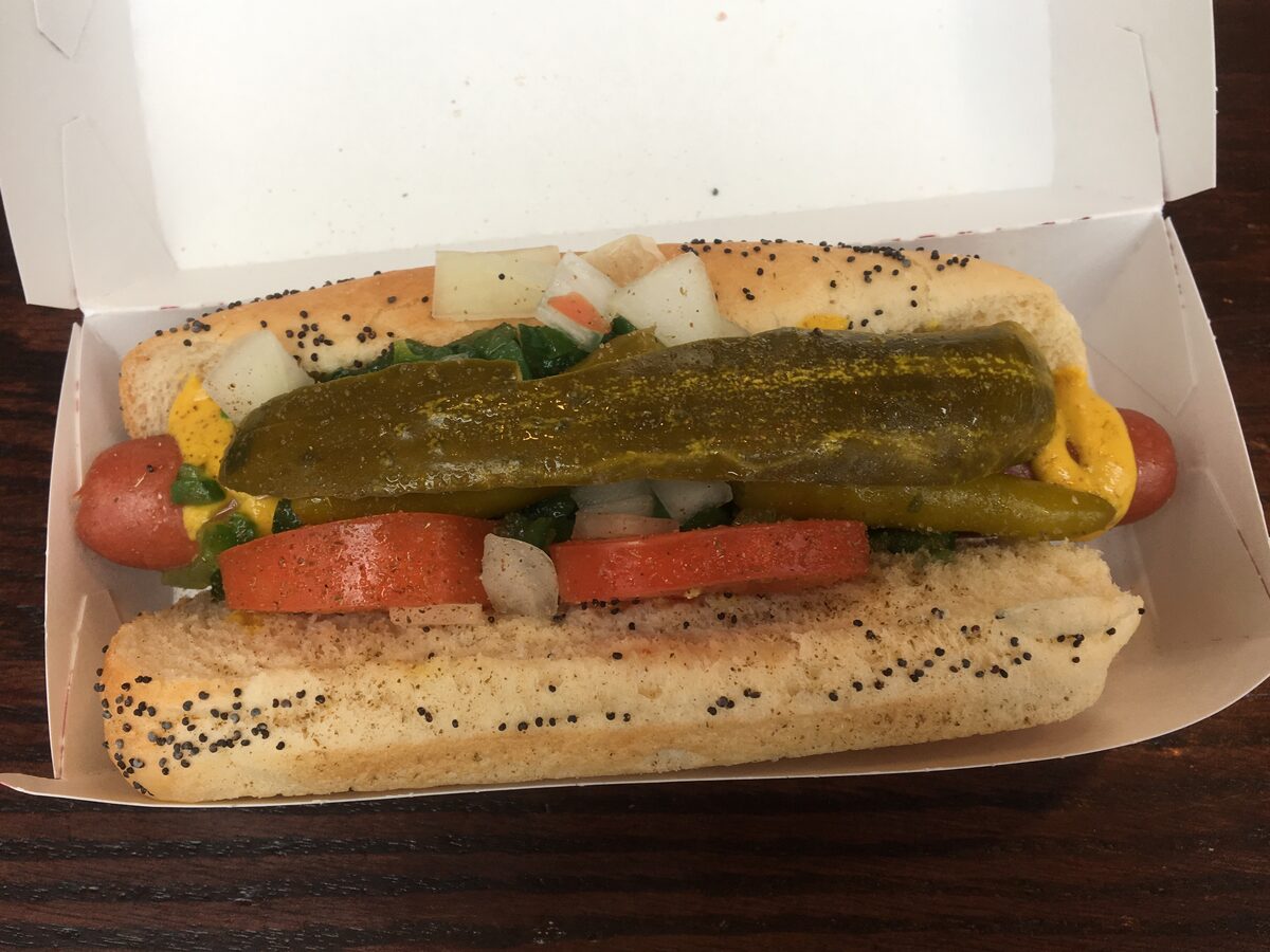 A Chicago-style hot dog on a poppy seed bun with a pickle spear, tomato slices, onion and peppers