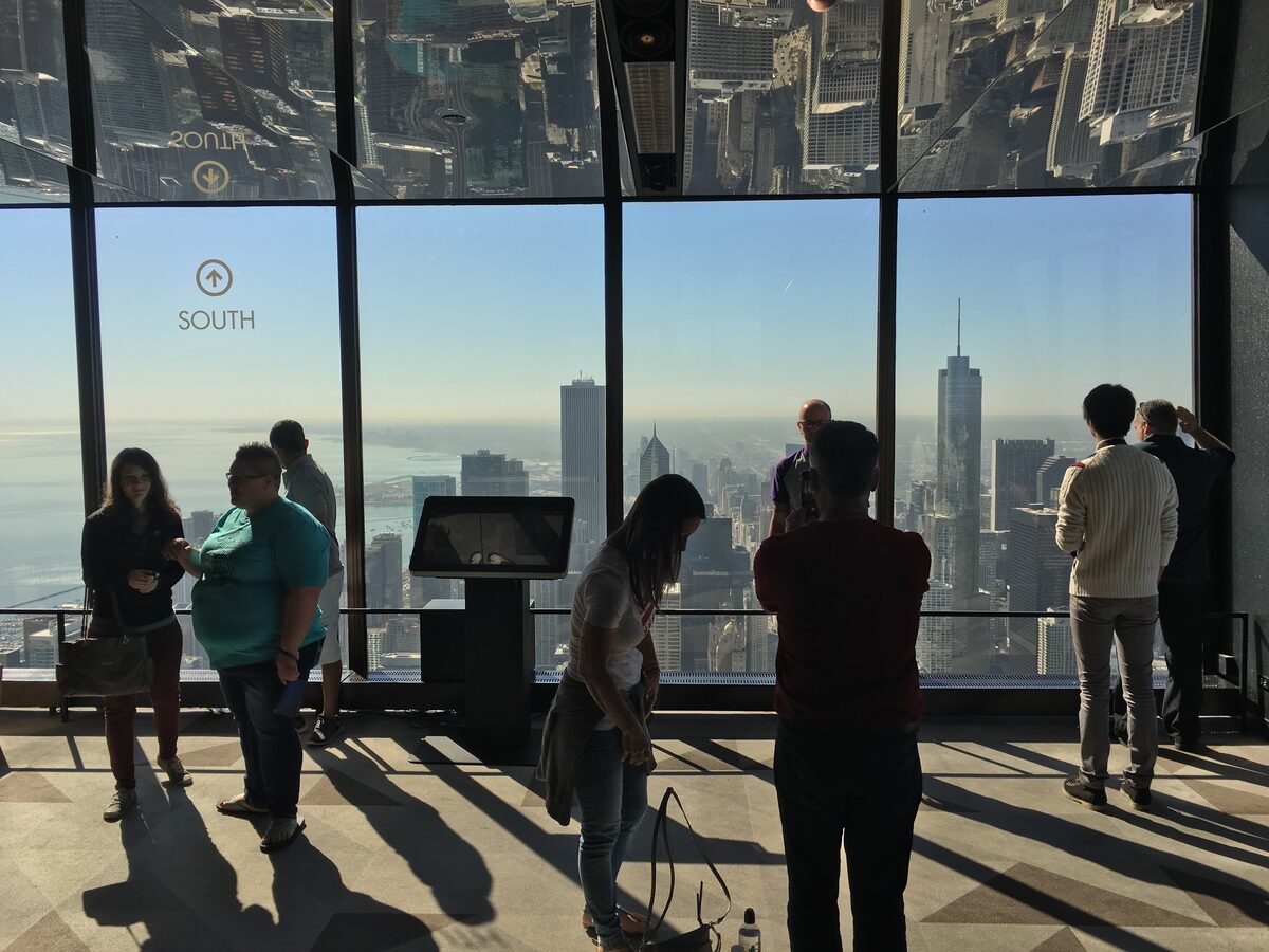 Visitors at the floor-to-ceiling windows of the 360 Chicago observation deck, skyline beyond